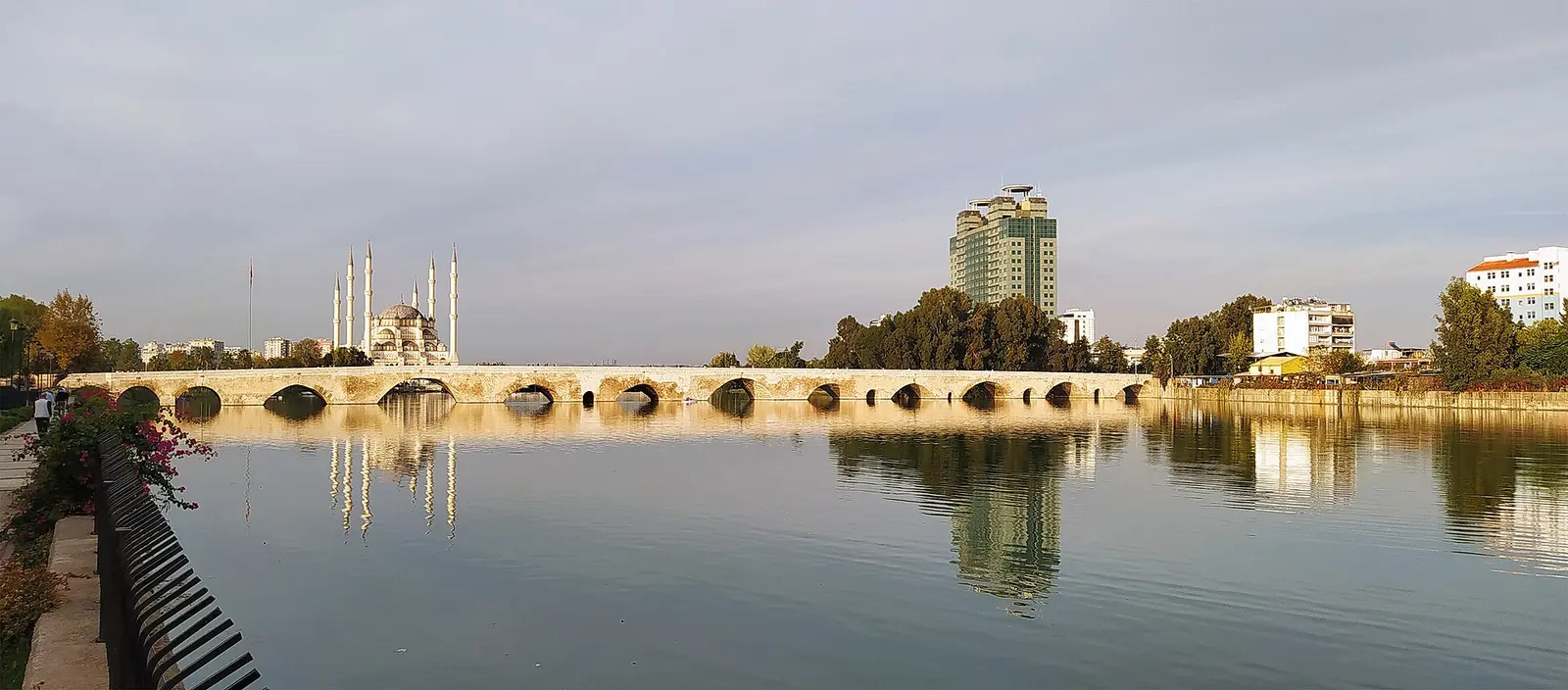 Roman stone bridge across the Seyhan River in Adana with a mosque and tall building behind